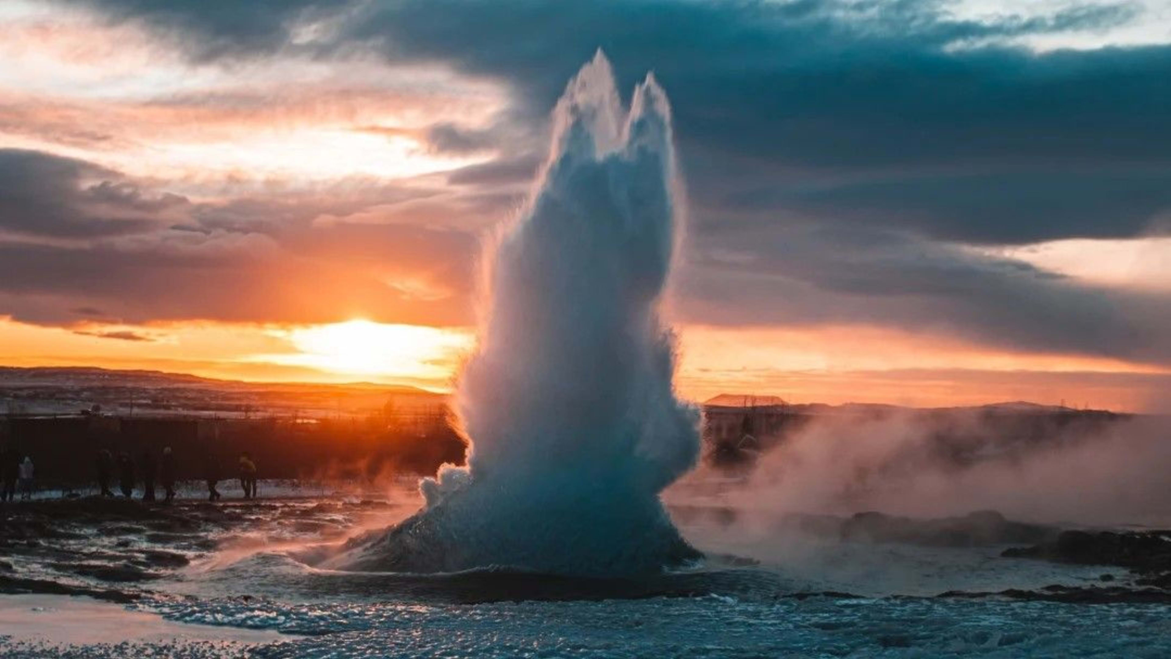 people watching geysir eruption at sunset