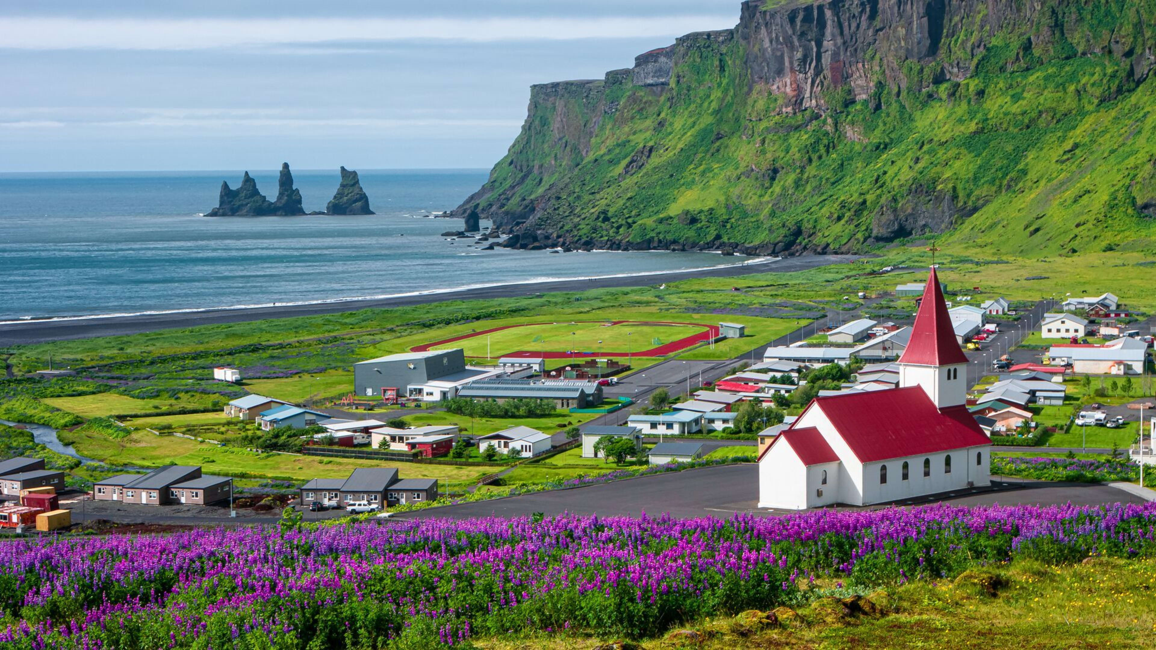 vik town in summer with its red church and reynisdrangar from distance