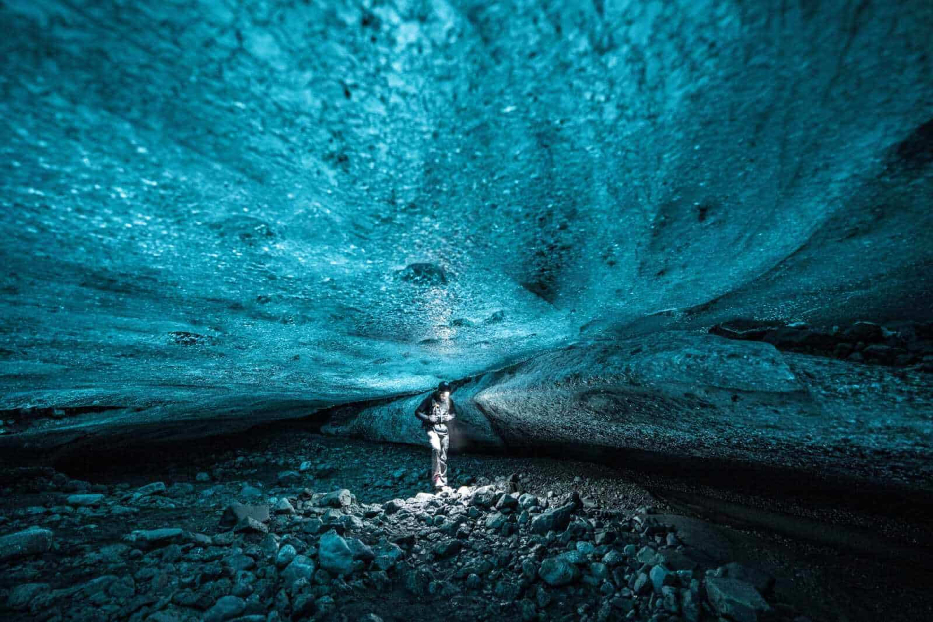 people standing under the great ice wall of the blue ice cave